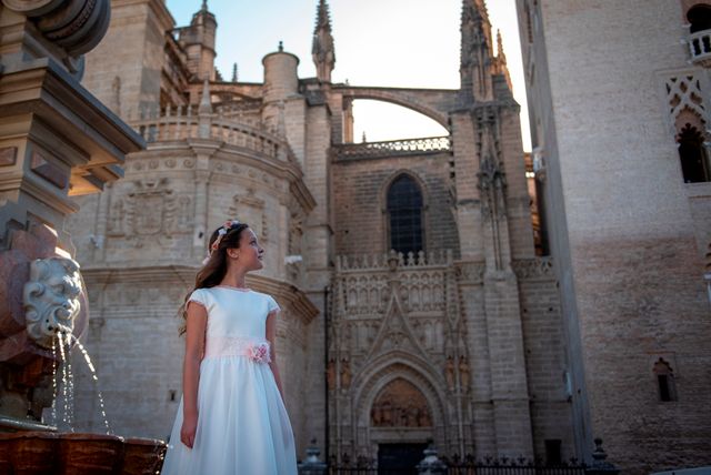 chica en vestido de comunión posando junto a una fuente frente a una catedral