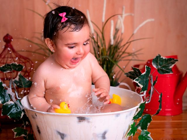 niña pequeña bañándose en un barreño con patos de goma