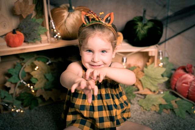 niña con diadema de orejas de ciervo y vestido a cuadros, haciendo una pose de terror frente a calabazas