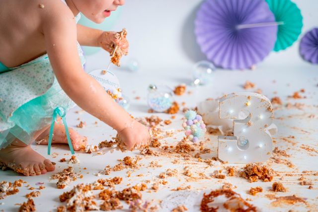 niña comiéndose con las manos un pastel destrozado, con un 3 de madera que representa su edad