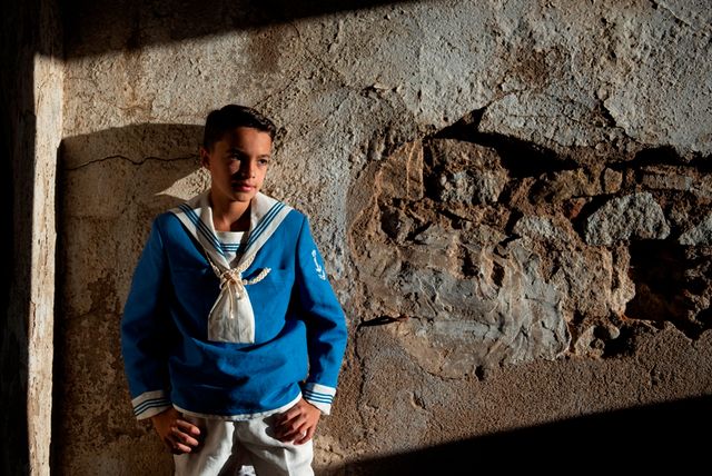 chico en traje de marinero de comunión posando en un muro de piedra