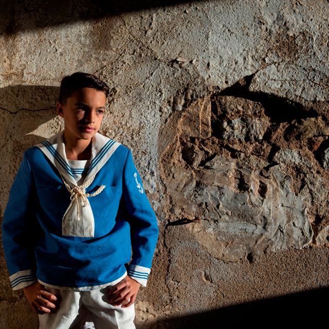 chico con traje de marinero de comunión apoyado en una pared de piedra