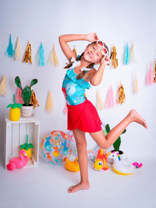 niña posando con ropa de verano y gafas de sol delante de juguetes