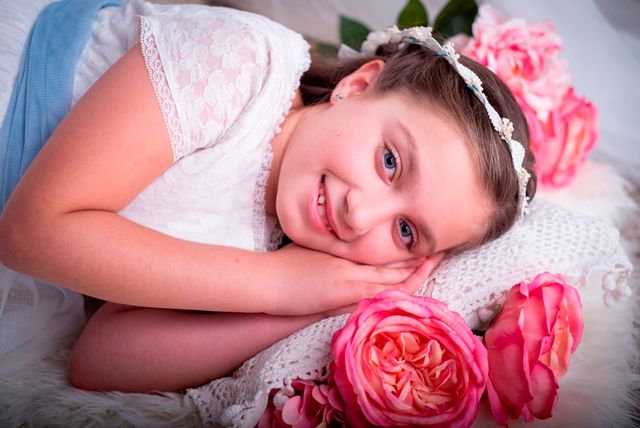 chica en vestido de comunión y diadema de rosas, posando tumbada en una cama