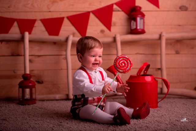 niño pequeño sosteniendo una piruleta junto a regadera roja