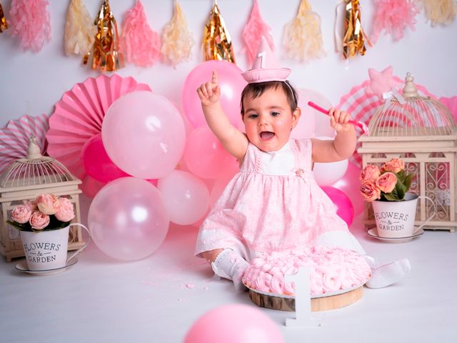 niña de 1 año con vestido rosa feliz junto a un pastel y globos rosas