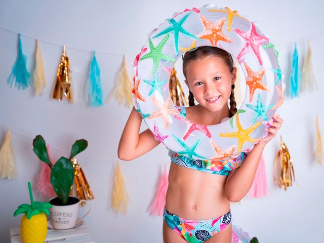 niña en bikini posando asomando la cara por el centro de un flotador