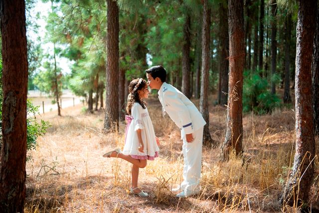 chico en traje blanco de comunión dando un beso en la frente a su hermana pequeña, en un pinar