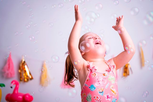 niña con dos coletas en bañador jugando con pompas frente a decoración veraniega