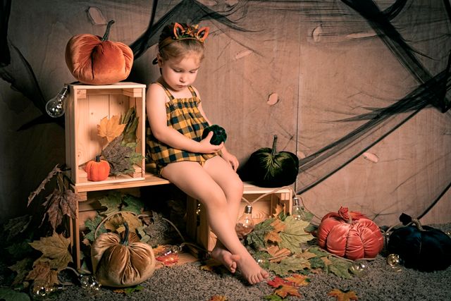 niña con vestido a cuadros sosteniendo un peluche junto a decoración de halloween