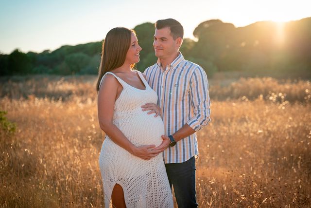 pareja embarazada posando en un campo de gramíneas al atardecer