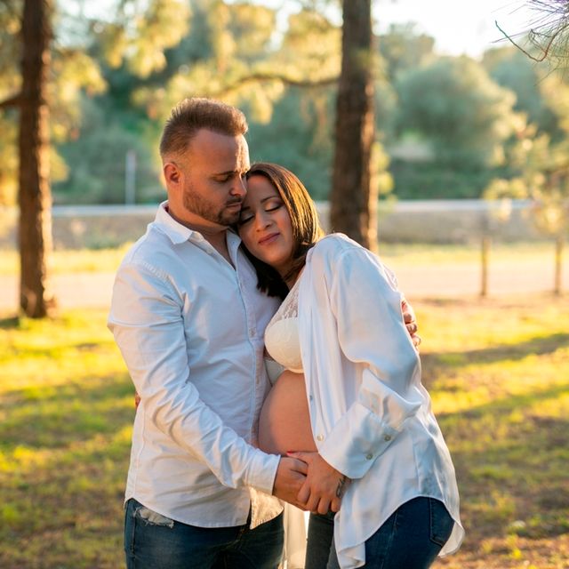 pareja vestida de blanco abrazada en un bosque, la mujer está embarazada