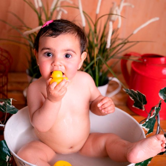 bebe comiéndose un patito de goma mientras se baña en un barreño