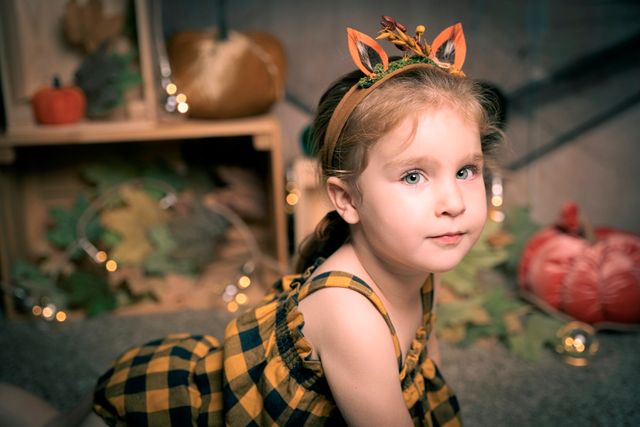 niña con diadema de orejas de ciervo y vestido a cuadros, posando frente a calabazas