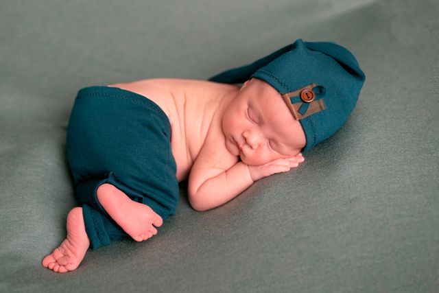 bebe con pantalones y pañuelo azules, durmiendo sobre superficie gris