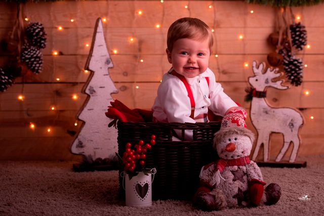 niño pequeño en una cesta de mimbre, junto a peluche de muñeco de nieve y fondo navideño