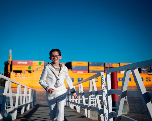 niño en traje de comunión de marinero subiendo por la pasarela de entrada de un barco