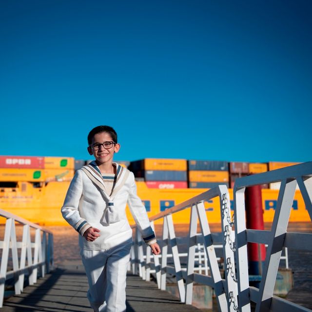 niño en traje de comunión de marinero subiendo por la pasarela de entrada de un barco