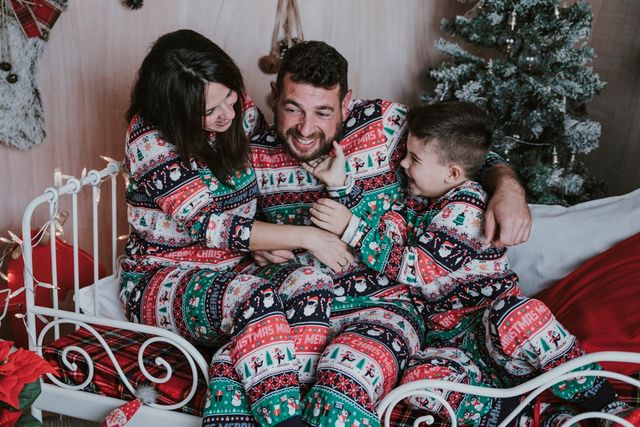 pareja con su hijo, todos vestidos con pijama navideño, sentados en la cama