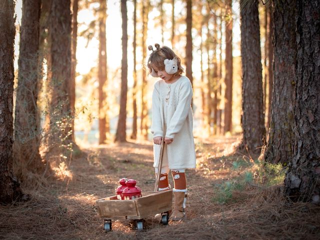 niña con vestido de lana blanco y orejeras de oso llevando dos farolillos rojos en una carretilla