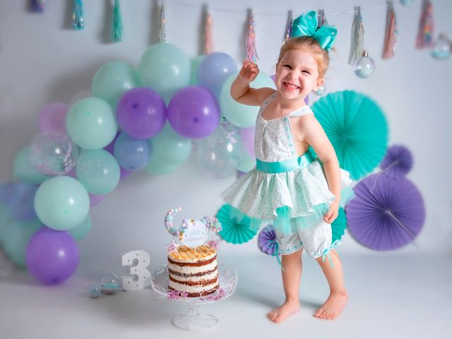 niña con vestido posando junto a globos, una tarta de cumpleaños y un 3 de madera