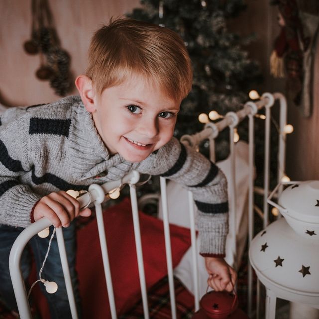 niño apoyado en el cabecero de una cama, con decoración navideña de fondo