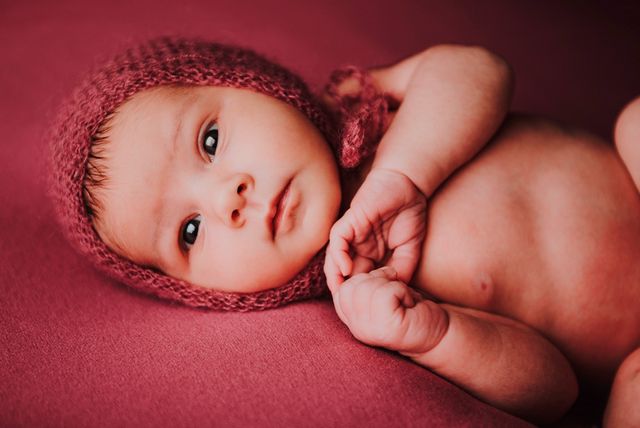 bebe con gorro de lana granate, tumbado sobre fondo granate