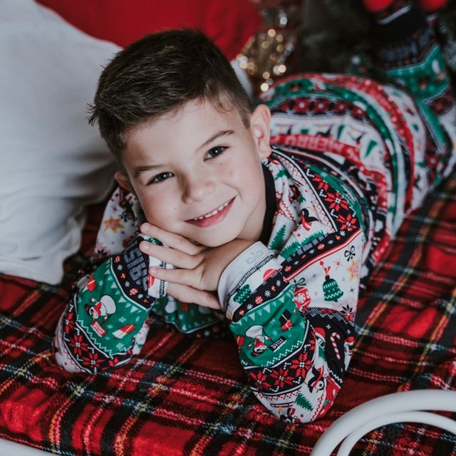 niño con jersey navideño tumbado sobre una cama con manta roja y verde a cuadros 