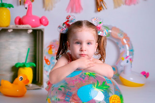 niña con dos coletas apoyada en flotador, de fondo decoración veraniega