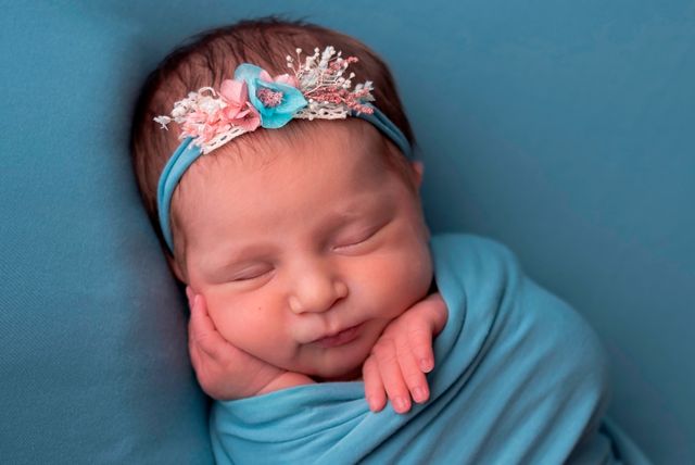 bebe con diadema de flores dormido envuelto en sábana azul, sobre fondo azul